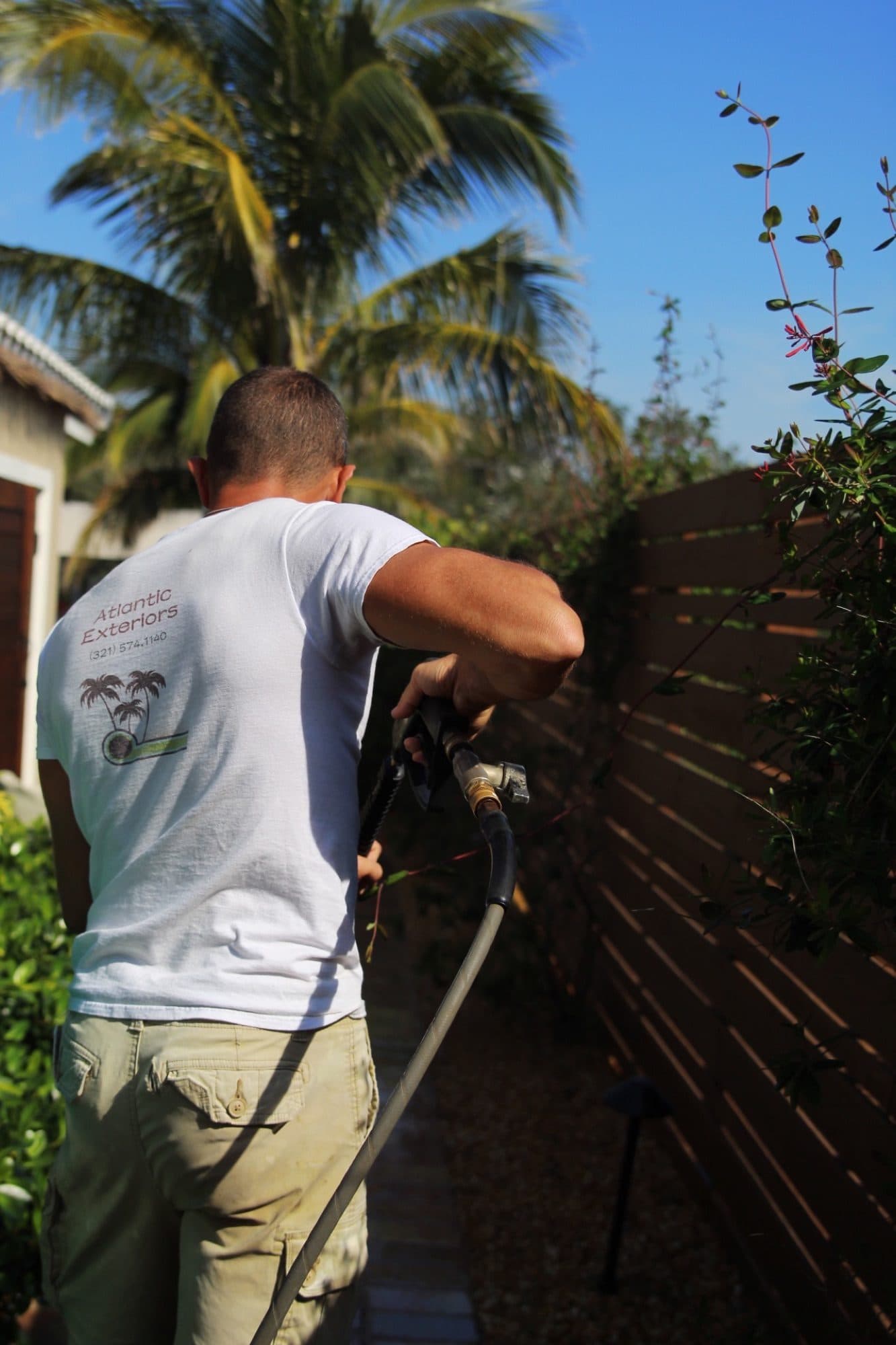 Derek spraying sealer along a fence line — paver work by Atlantic Exteriors in Brevard County, FL