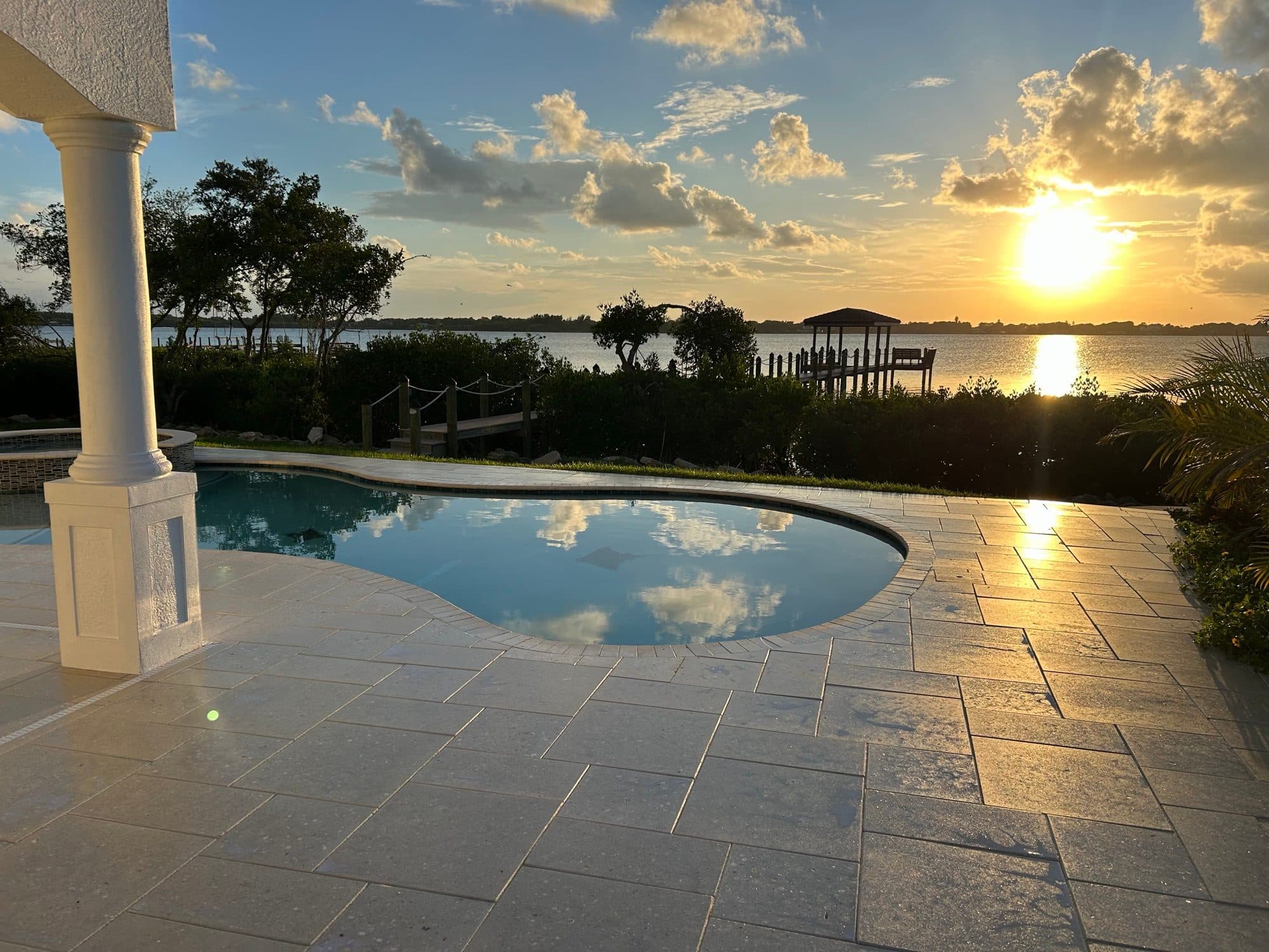 Sealed waterfront travertine pool deck at sunset in Brevard County, FL — pool deck paver sealing by Atlantic Exteriors